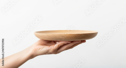 Close up view of a human hand holding a plain empty wooden plate isolated on a white background