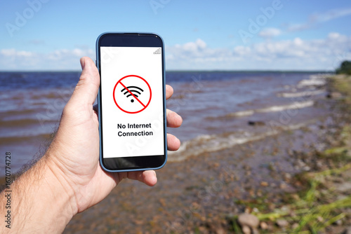 Hand holding smartphone showing no internet connection at the beach