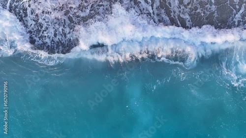 A mesmerizing 4K top-down drone shot of a powerful white wave cresting and breaking on a pristine sandy beach creating a beautiful and energetic natural display of the ocean's force