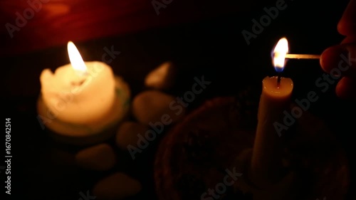 Woman lights a candle with a match on dark black background in holiday celebration. Candle burning fire flame with space. Magic ritual candle. Close-up romantic decor