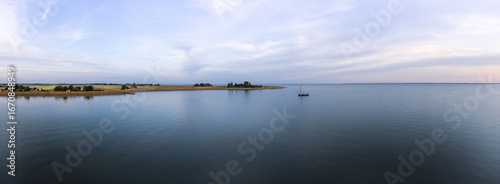 Tranquil evening panoramic aerial view of a tjalk ship with furled sails nestled on Markermeer lake near a rural village Schellinkhout in the Netherlands, surrounded by serene water and a calm horizon