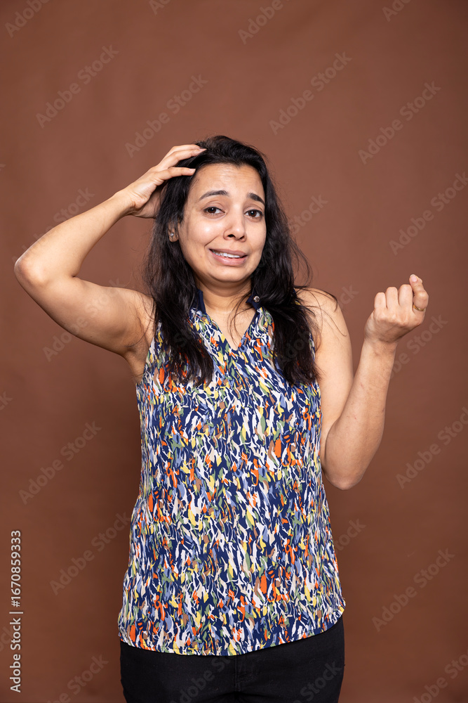 Fototapeta premium Female individual with hand on head, trying to remember something, expressing forgetful moment. Gorgeous woman in casual outfit, looking disoriented while standing against isolated background.