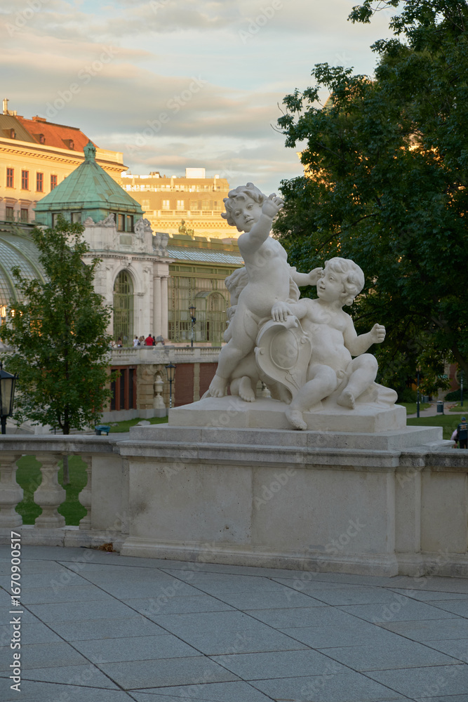 Obraz premium Sculpture of two infant cherubs in Vienna’s Palm House garden, highlighting detailed craftsmanship, classical design, and serene outdoor ambiance.