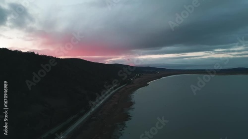 Pink sky's over the mountains as the highway runs along the dark waters edge below.