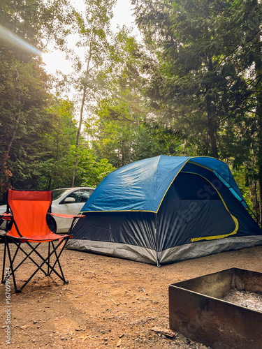 Wide view of large campsite with glowing campfire, parked cars, and camping gear.