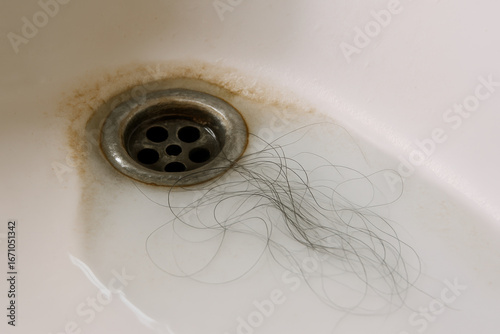Loose dark hair tangled near rusty bathroom sink drain, concept of clogged pipes, personal hygiene or hair loss issues