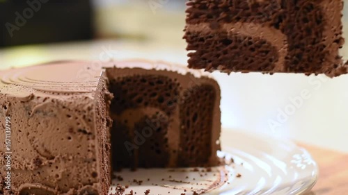 Close up of a slice being removed from a chocolate cake on a clear glass serving plate cake stand