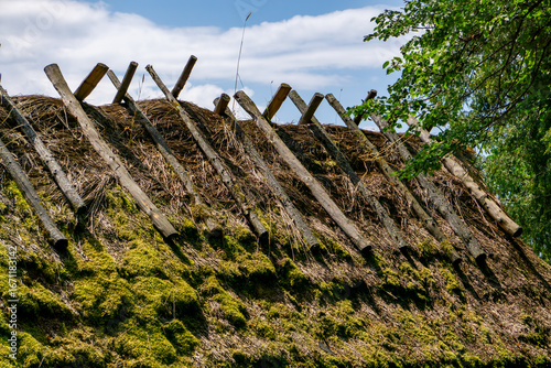 Foto Thatched roof covered with moss, reinforced with wooden poles, visible fragment of traditional rural architecture