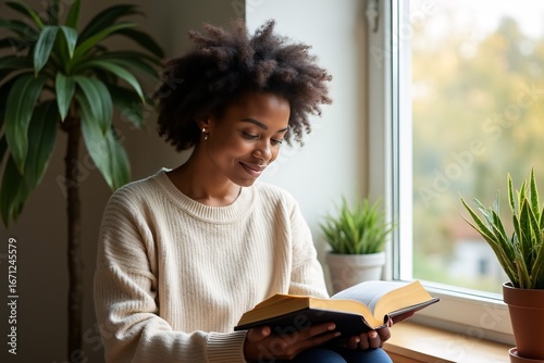 Young African American Woman Reading Open Bible by Window in Warm Light - Peaceful Atmosphere