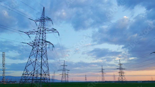 Quadro em tela Power lines and pylons silhouette against a dusk sky in soft blue and pink, symbolizing sustainable energy infrastructure and modern power distribution, captured in a full-length shot