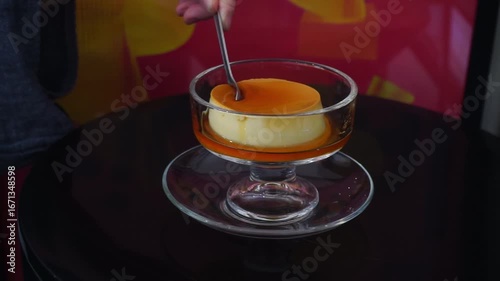 A woman's hand picks up a spoon and scoops up caramel custard pudding