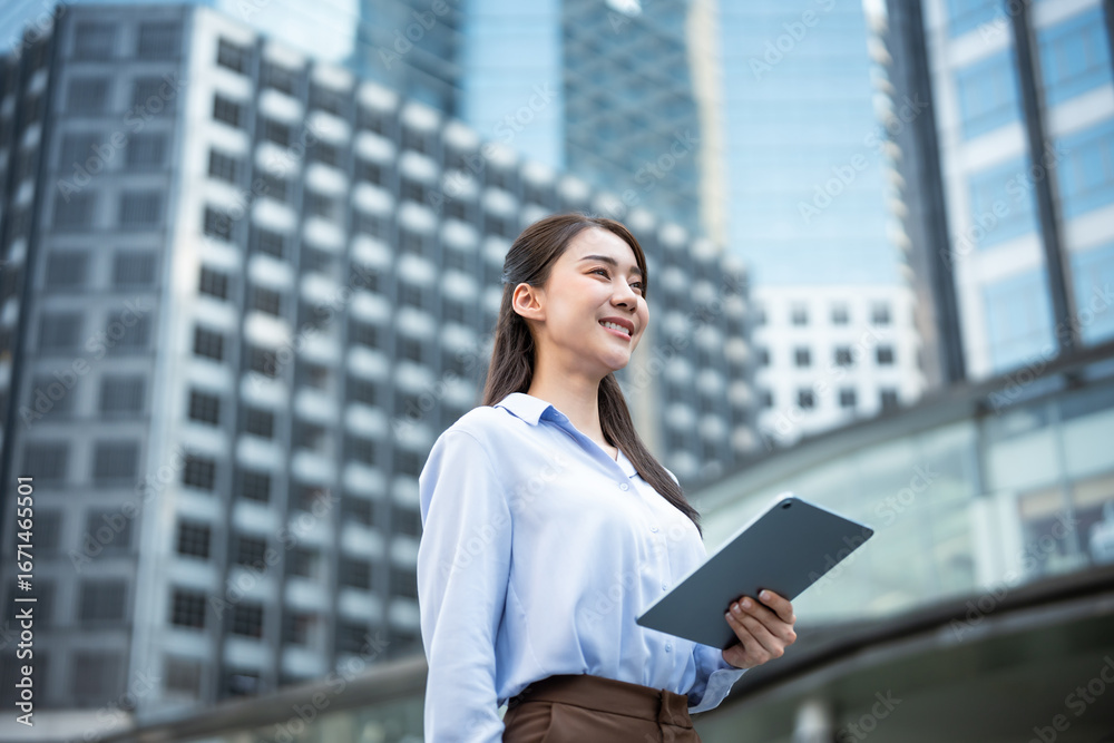 Fototapeta premium Asian young businesswoman using digital tablet while standing in the city. 