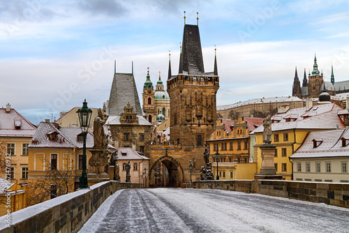 Photography Scenic winter view of Charles Bridge in Prague with historic statues, snowy pathway, and gothic towers
