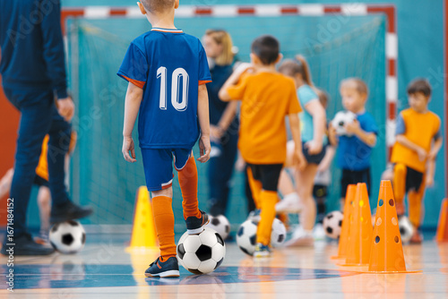 Football futsal training for children. Sport background. Soccer training dribbling cone drill. An indoor soccer young player with a soccer ball in a sports hall. Players in blue and  orange uniforms