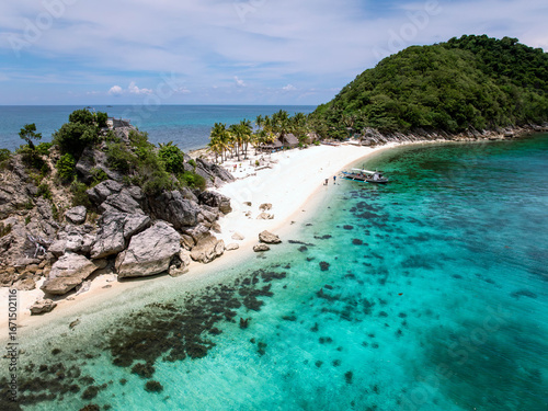 Aerial view of the turquoise waters meeting the white sandy beach and lush green island, a tropical paradise unfolds from above, Caramoan, Camarines Sur, Philippines.
