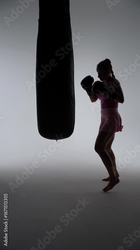 Kickboxing, woman pro fighter trains his punches, beats a punching bag, training in the dark boxing gym, strength fit body, strikes fast, contour light silhouette.