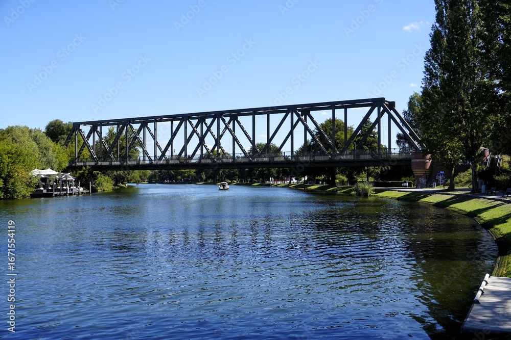 Fototapeta premium Scenic landscape panorama of a boat crossing the historic railway bridge over river Havel in Caputh, Brandenburg, Germany