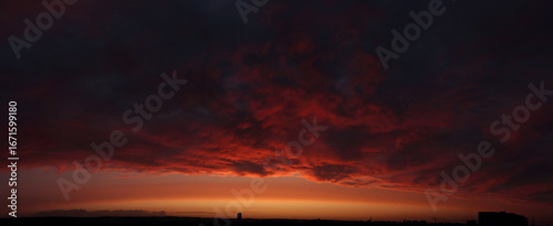 High resolution stormy sunset panorama. Dark clouds highlighted red and gold by setting sun, golden arch above horizon.
