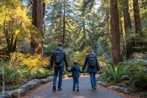 A family walks hand-in-hand along a scenic path through a lush, sunlit forest surrounded by tall trees and greenery