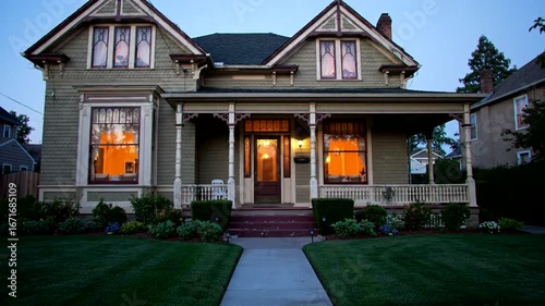 Elegant vintage house with illuminated windows, surrounded by a lush lawn, creating a cozy evening atmosphere.