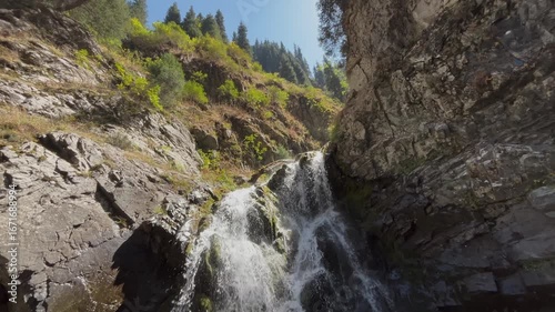 Beautiful panorama of a mountain waterfall with several cascades. Scenic wilderness landscape with flowing water, rocky terrain, coniferous forest, and natural beauty of pristine highland nature captu