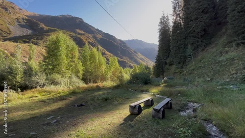 Beautiful mountain landscape at sunrise with wooden benches in the foreground. Coniferous forest and mountain peaks in the background create a peaceful outdoor atmosphere of wilderness, relaxation, an