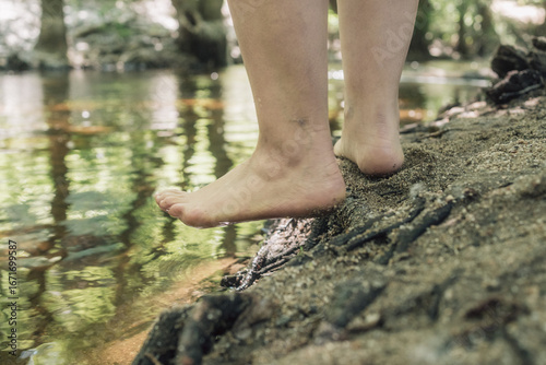 Woman with lipedema entering river in forest, testing water with foot