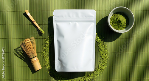 Minimalist Flat Lay of Matcha Tea Powder Packaging and Traditional Bamboo Whisk on Green Mat.