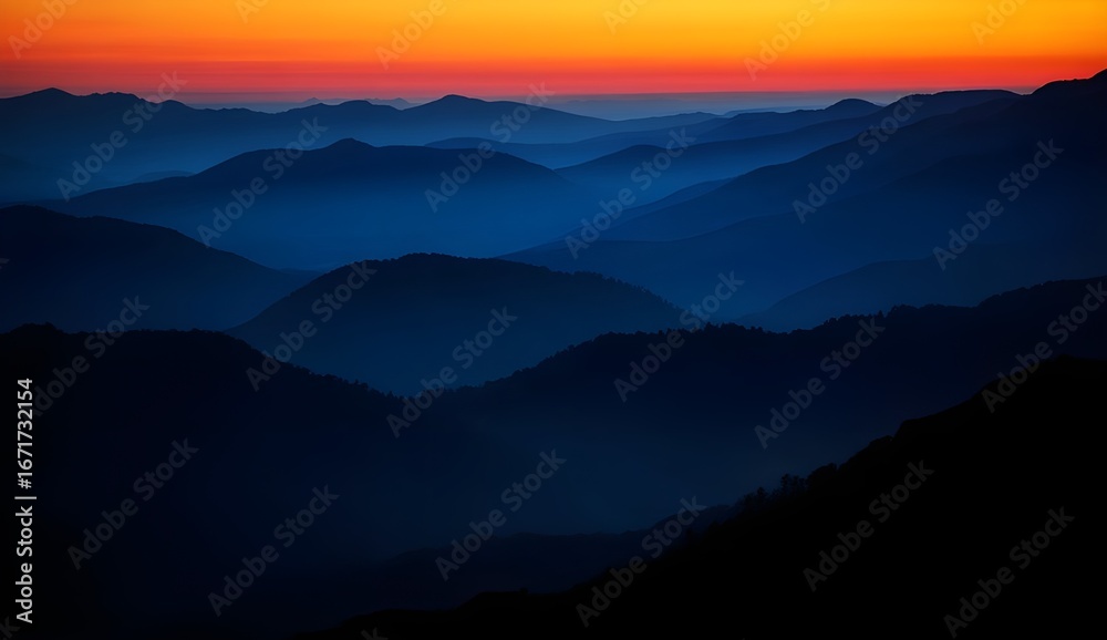 Naklejka premium Dramatic mountain landscape at sunset with vibrant orange sky and blue mist