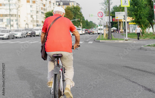 Elderly man cycling on urban street during daytime with city buildings in background