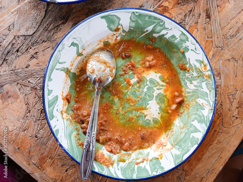 An empty plate with leftover food, beans, and sauce, showing remnants of a finished meal with a spoon.