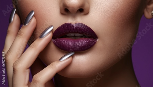 Close-up of lips painted in matte dark purple lipstick, gently touched by fingers with long metallic silver nails. perfect for premium stock use in makeup, accessories, and luxury design.