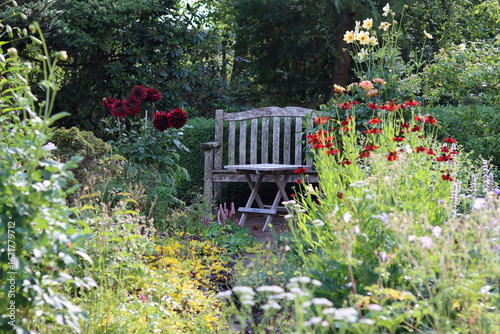 Seat and table in a garden surrounded by flower beds full of heleniums and dahlias in late summer