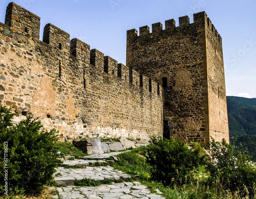 A large, imposing stone fortress stands tall against a clear blue sky, showcasing intricate battlements and a formidable tower.