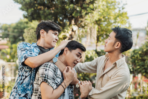 A distressed young Asian man is grabbed in a rear chokehold by a bully while another aggressor confronts him up close with intimidation.