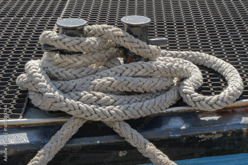 Fototapeta premium Thick braided mooring rope tied around a black cleat on a dock, detailed maritime equipment close-up