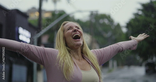 Woman raising arms and looking upward in rain, overwhelmed with joy, gratitude, and emotional catharsis