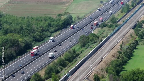 Aerial view of busy Italian highway A1 with trucks and cars traveling on a sunny day. Traffic flows along the Autostrada del Sole, a major Italian transport artery, showcasing the movement of goods