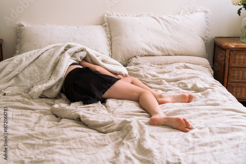 Relaxed girl lying in bed with a soft duvet partially covering her. Peaceful and cozy moment in a minimalist bedroom with natural linen bedding.	
