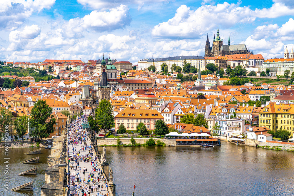 Obraz premium Prague from above the historic quarters of Mala Strana, Charles Bridge, Prague Castle, and the calm waters of the Vltava River framed by summer greenery and a blue sky.Prague,Czech Republic.