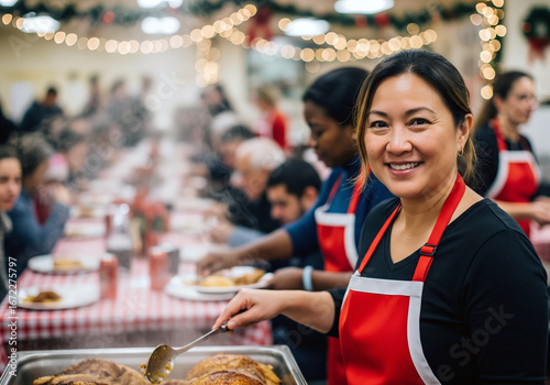 A smiling female volunteer looks directly at the camera while serving a hot holiday meal from a large tray at a bustling community event.