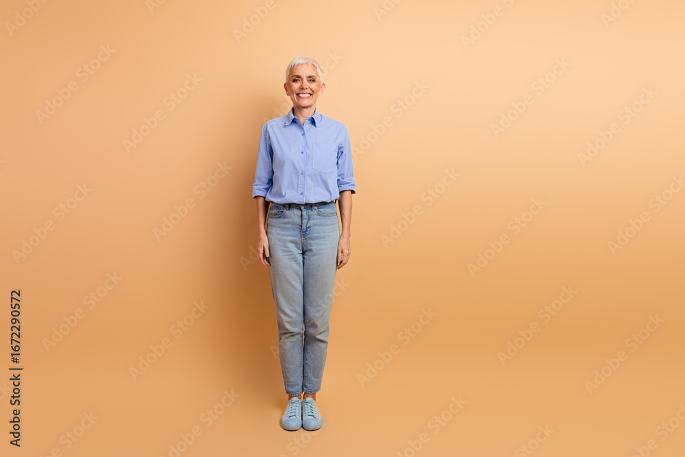 Fototapeta premium Charming Stylish Mature Woman Poses in Casual Fashion on Beige Background