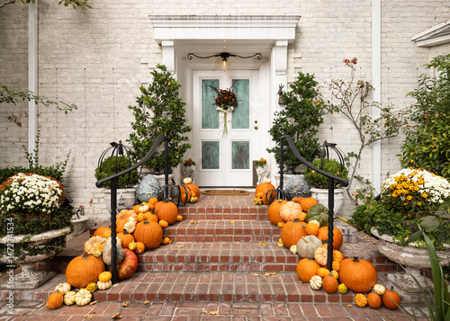Fall, autumn in beautiful American suburban brick home with stairway entrance, leaves, and variety of pumpkins and gourds arranged artfully as decoration