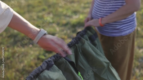 Two individuals work closely together to set up a tent outdoors, surrounded by lush greenery and nature