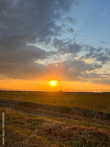 Sunset over golden fields with fence and colorful sky, A golden sunset over a grassy prairie with a rustic wooden fence,  Sunset over a barbed wire fence and rural field, golden light.