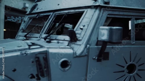 Armored vehicle exhibiting perforations from projectiles, conceptual theme relating to criminal activity and violent extremism.