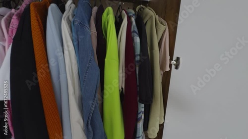 A first-person perspective POV video shows a man's hands opening a modern, light-colored wardrobe. The camera, positioned over the shoulder, captures his hand reaching into the organized closet