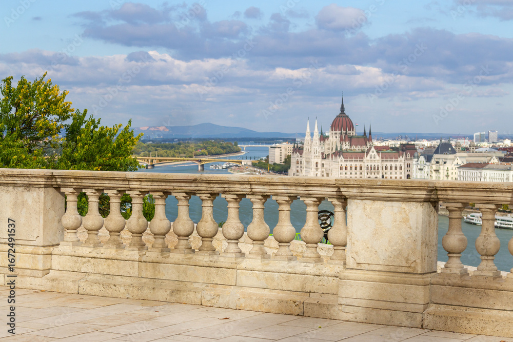 Fototapeta premium Panoramic view from Savoy Terrace with decorative stone balustrade overlooking Danube River and Hungarian Parliament building under sunny blue sky. Budapest, Hungary.