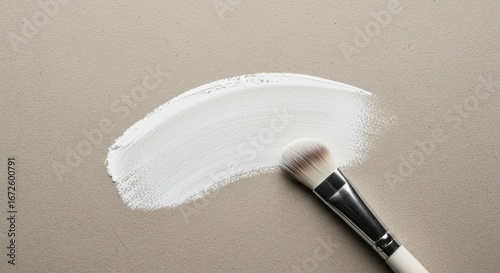 A delicate white paint stroke rests upon a neutral backdrop, accompanied by a matching paintbrush.