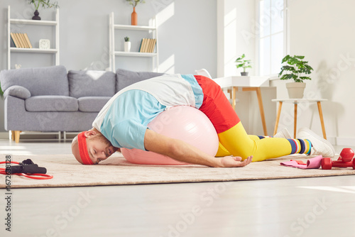 Foto Funny tired man in colored sports clothes lying on the yoga ball with his eyes closed